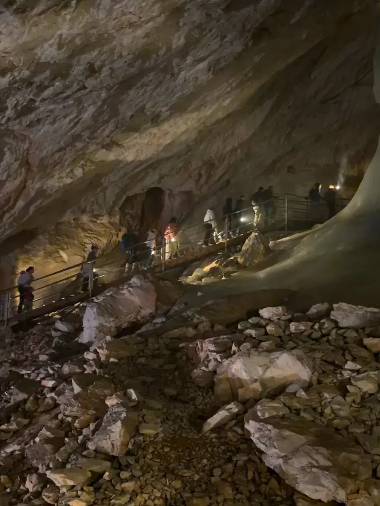 Visitors walking along a metal walkway inside Eisriesenwelt Ice Cave in Werfen, Austria, illuminated by small lights.