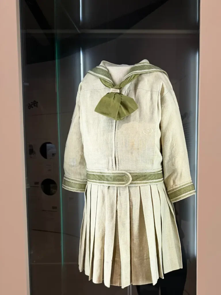 Gretl's cream-colored school uniform with green trim and a matching bow from The Sound of Music, displayed at the Sound of Music Museum in Salzburg.