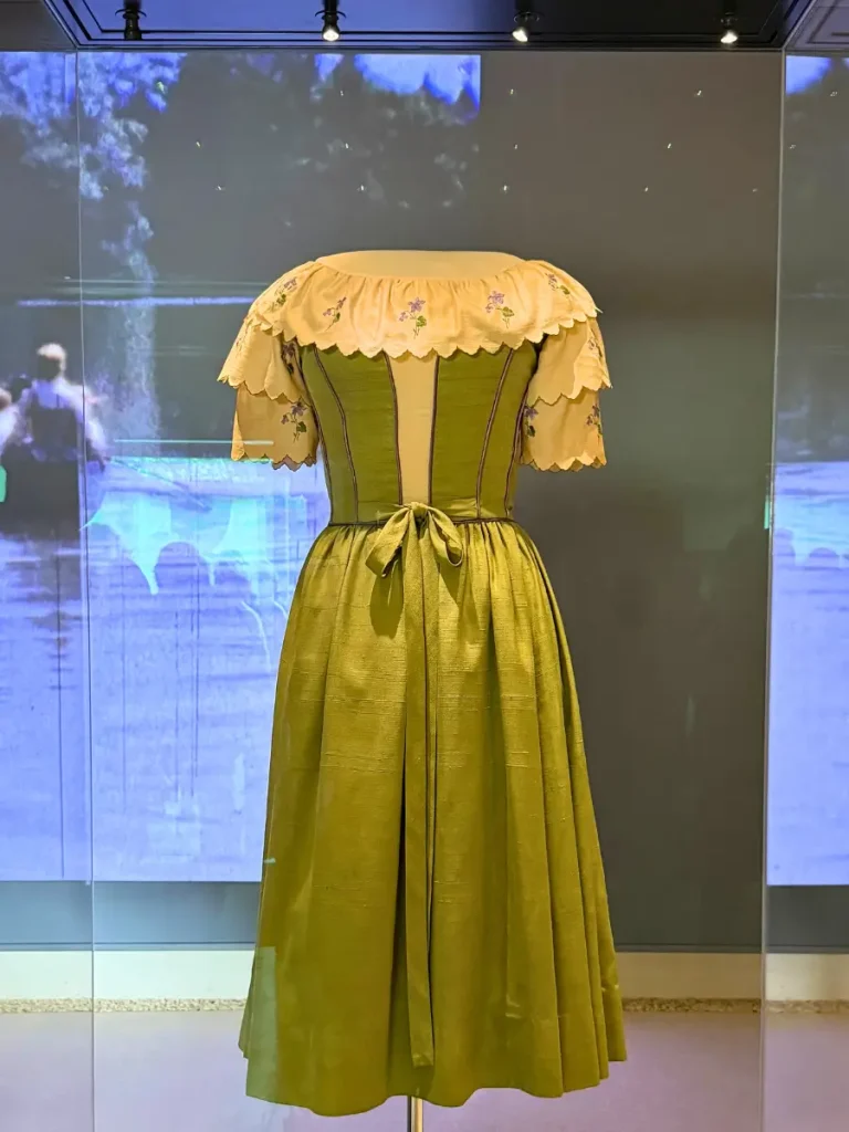 Green dress with embroidered cream sleeves worn by Liesl in The Sound of Music, displayed inside a glass case at the Sound of Music Museum in Salzburg.