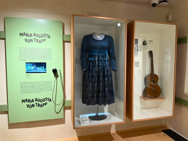 Maria von Trapp's winter drindl and acoustic guitar displayed in glass cases at the Sound of Music Museum in Salzburg, Austria.