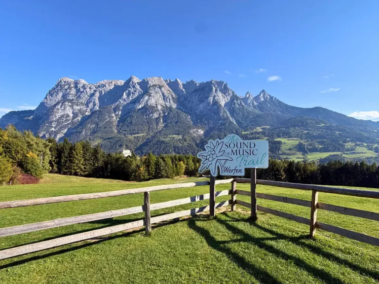 Sound of Music Trail sign in a fenced grassy meadow overlooking the Austrian Alps in Werfen, Austria.