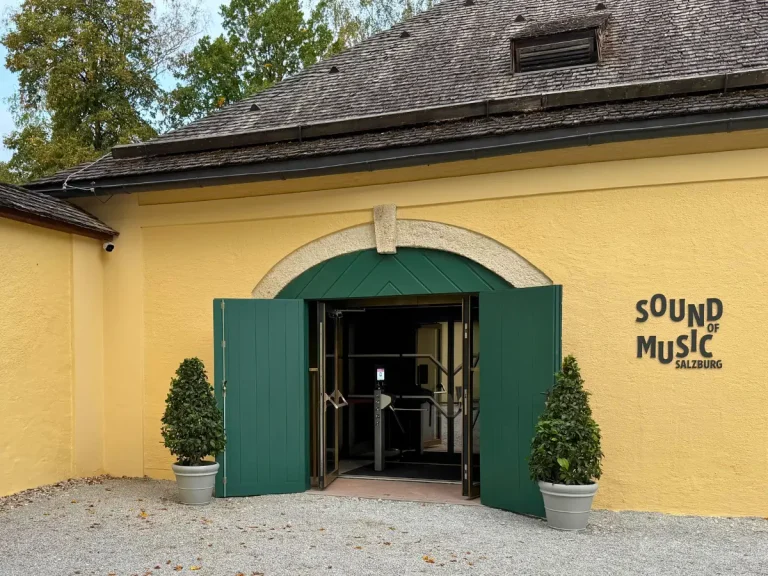 Entrance to the Sound of Music Museum at Hellbrunn Palace in Salzburg, featuring green doors and the museum's logo on a yellow building.
