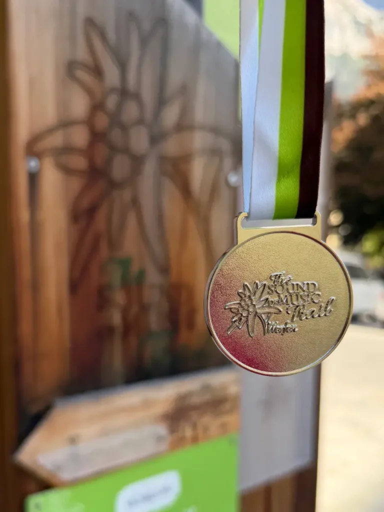 Close-up of the gold Sound of Music Trail completion medal from Werfen, Austria, hanging from a green, white and burgundy ribbon.