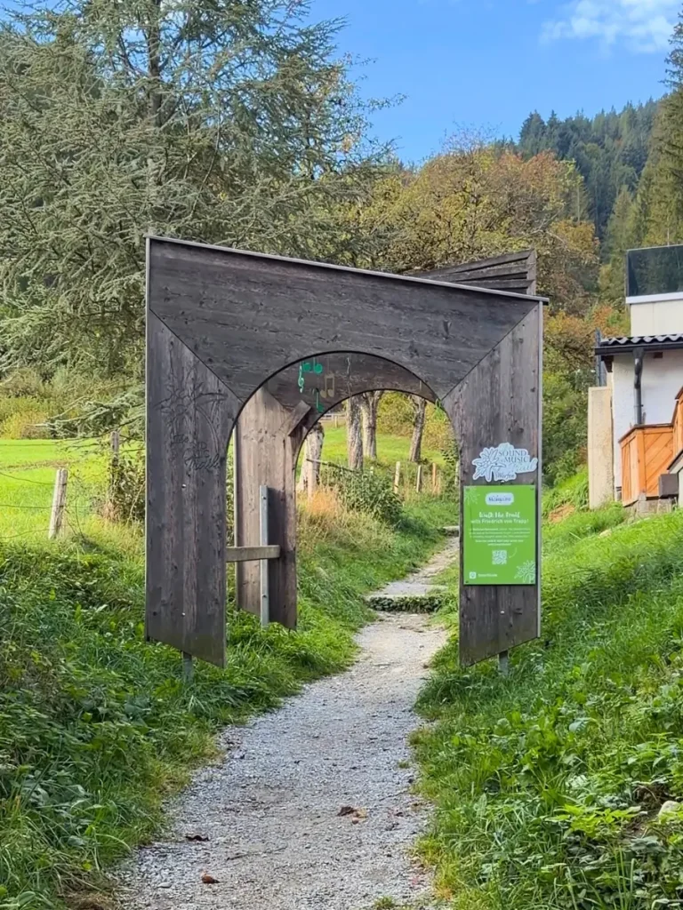 Wooden Sound of Music Trail entrance archway over a gravel hiking path surrounded by trees and green grass in Werfen, Austria.