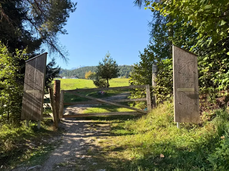 losed wooden gate between two Sound of Music Trail information signs, with a grassy field and mountains in the distance.