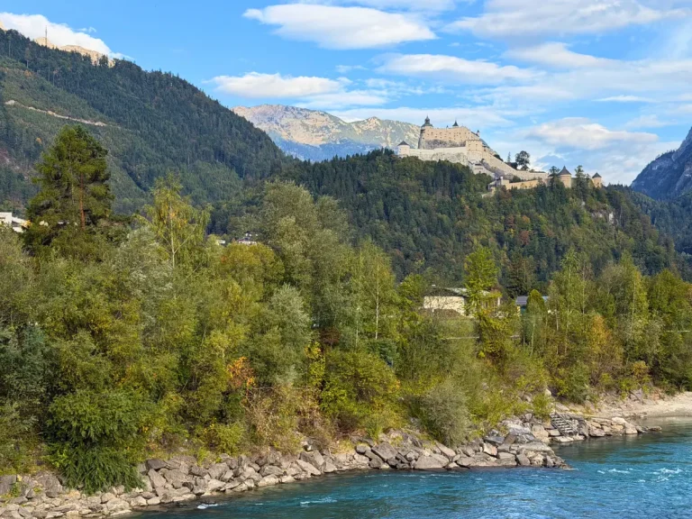 Hohenwerfen Fortress overlooking the Salzach River in Werfen, Austria, with forested hills and the Austrian Alps in the background.