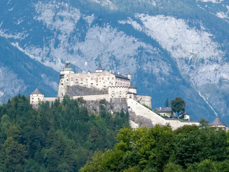 Burg Hohenwerfen, a medieval fortress perched on a forested hill in Werfen, Austria, with the Austrian Alps rising behind it.