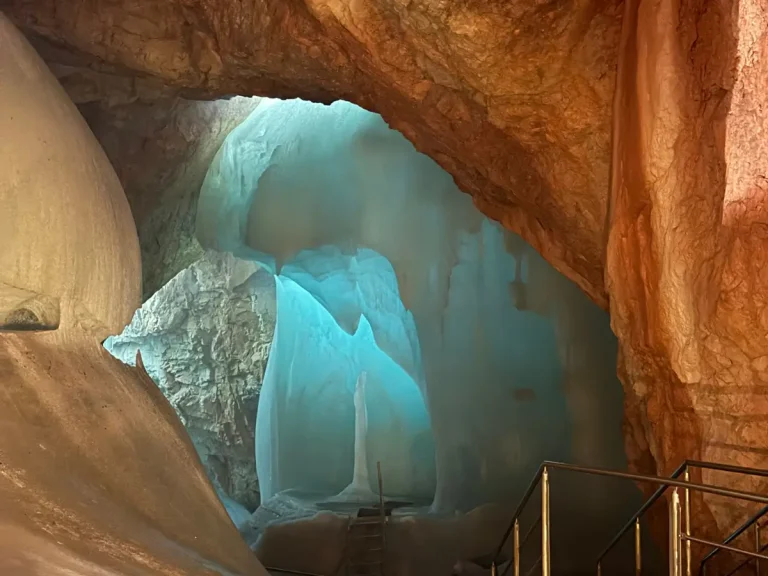 Blue ice formations inside Eisriesenwelt, the world's largest ice cave, in Werfen, Austria, surrounded by rocky walls and a metal stairway.